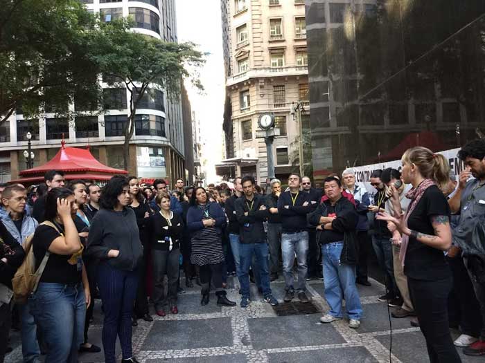 Foto da bancária, representante sindical, Thais Menezes, falando ao microfone com outros trabalhadores em volta