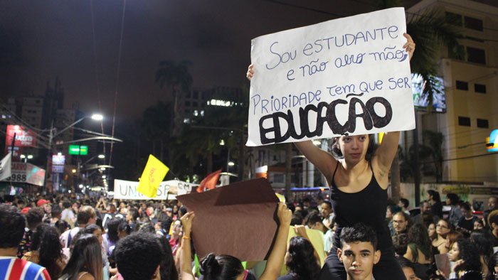Foto do ato do dia 15/05. Garota segura cartaz escrito: "Sou estudante e não abro mão, prioridade tem que ser EDUCAÇÃO"